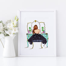 Framed artwork of a woman sitting at a vanity mirror with flowers on a white surface.